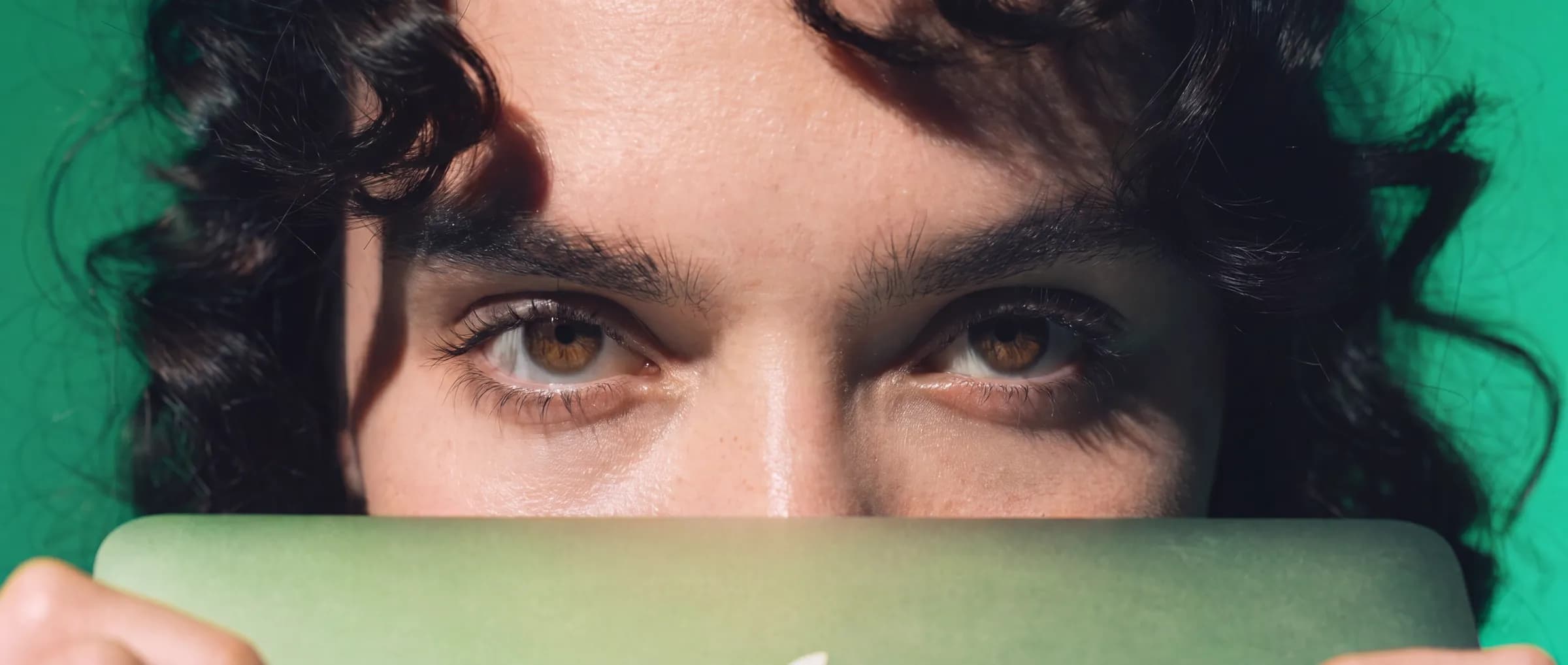 Primer plano de la mirada de un estudiante asomando tras un portátil verde